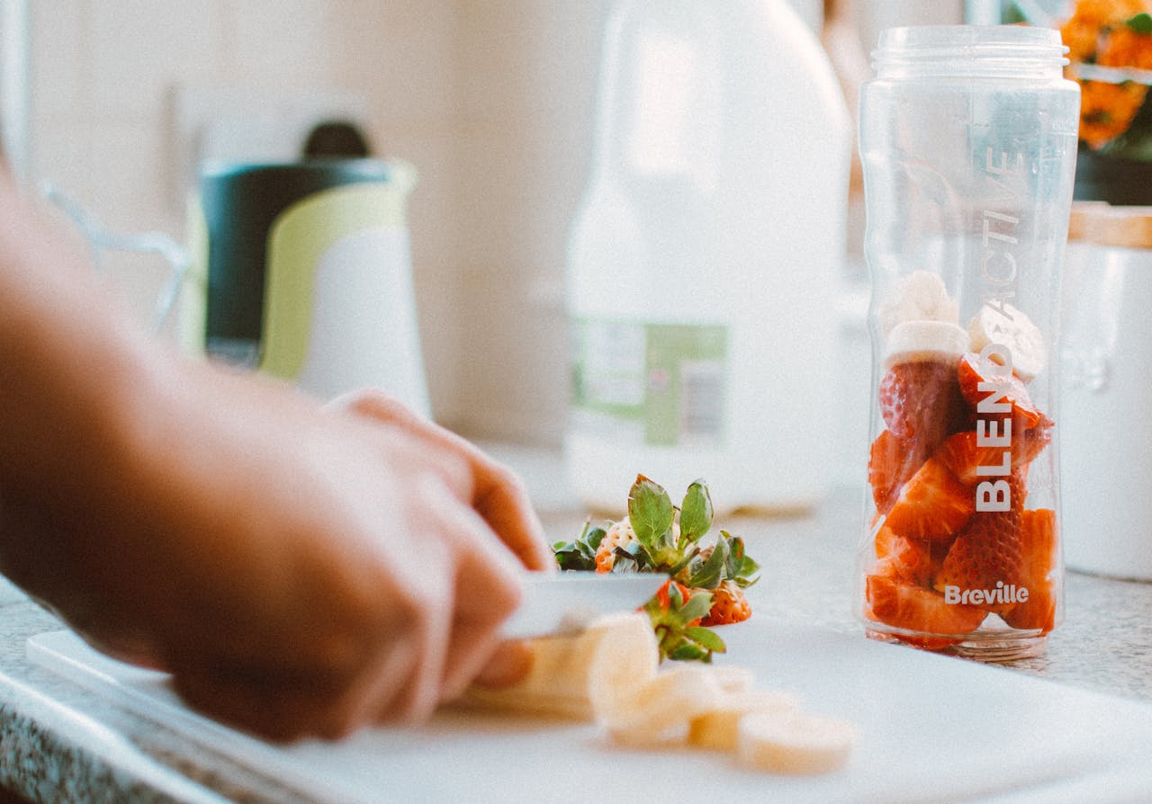 Close-up of hands slicing fruits for a nutritious smoothie, emphasizing health and freshness.